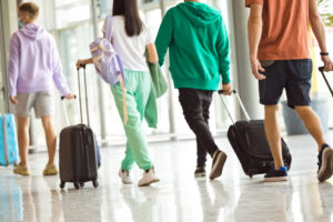 Back view of people traveling by plane, carrying luggage in airport terminal.